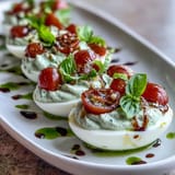 Creamy Caprese Deviled Eggs glistening with basil oil and colorful diced toppings.
