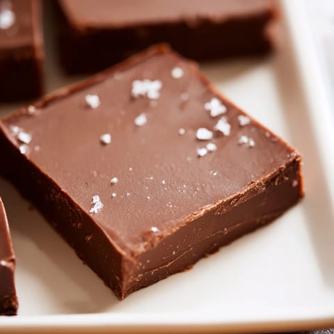 A close-up of glossy, dark chocolate fudge cooling after being freshly made in a pan.