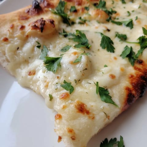 Fresh parsley garnish and Parmesan cheese top this savory Creamy Garlic White Pizza, served hot and ready to slice.