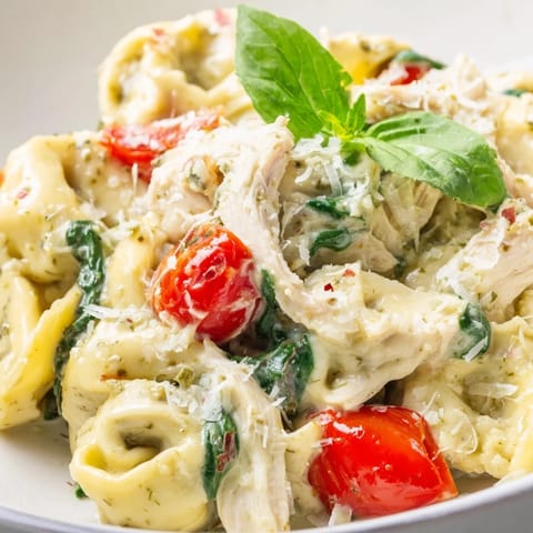 Creamy Pesto Tortellini Skillet features tender pasta and shredded chicken in a vibrant green sauce, garnished with cherry tomatoes and fresh basil.