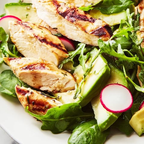 Golden grilled chicken slices rest atop vibrant mixed greens, crisp cucumber ribbons, and sharp pink radish slices, all glistening with a freshly whisked lemon vinaigrette.
