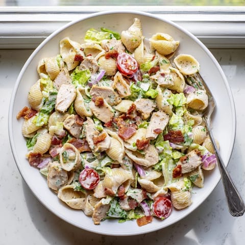 Hearty BLT Chicken Pasta Salad served in a white bowl, featuring tender pasta shells and chopped romaine.