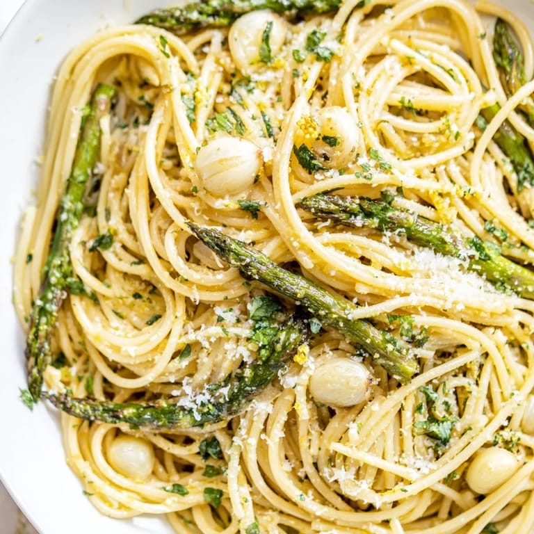 A close-up of Roasted Garlic & Asparagus Pasta shows glossy olive oil, tender spears, and melted Parmesan clinging to every strand.  
