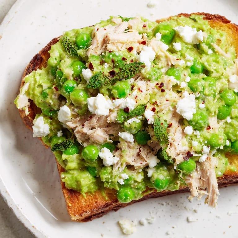 A vibrant open-faced Smashed Pea & Chicken Toast garnished with chili flakes, ready to serve warm.