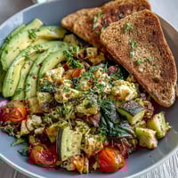 A close-up of a fluffy Egg and Vegetable Scramble in a skillet, featuring diced red bell peppers, spinach, and cherry tomatoes.  