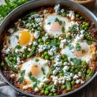 Spring-inspired Pea and Broad Bean Shakshuka with runny yolks served from a hot skillet.
